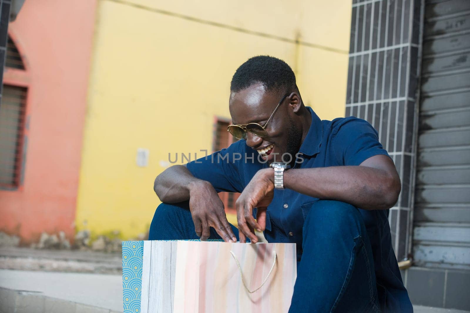 young man sitting outdoors looking in shopping bag smiling.