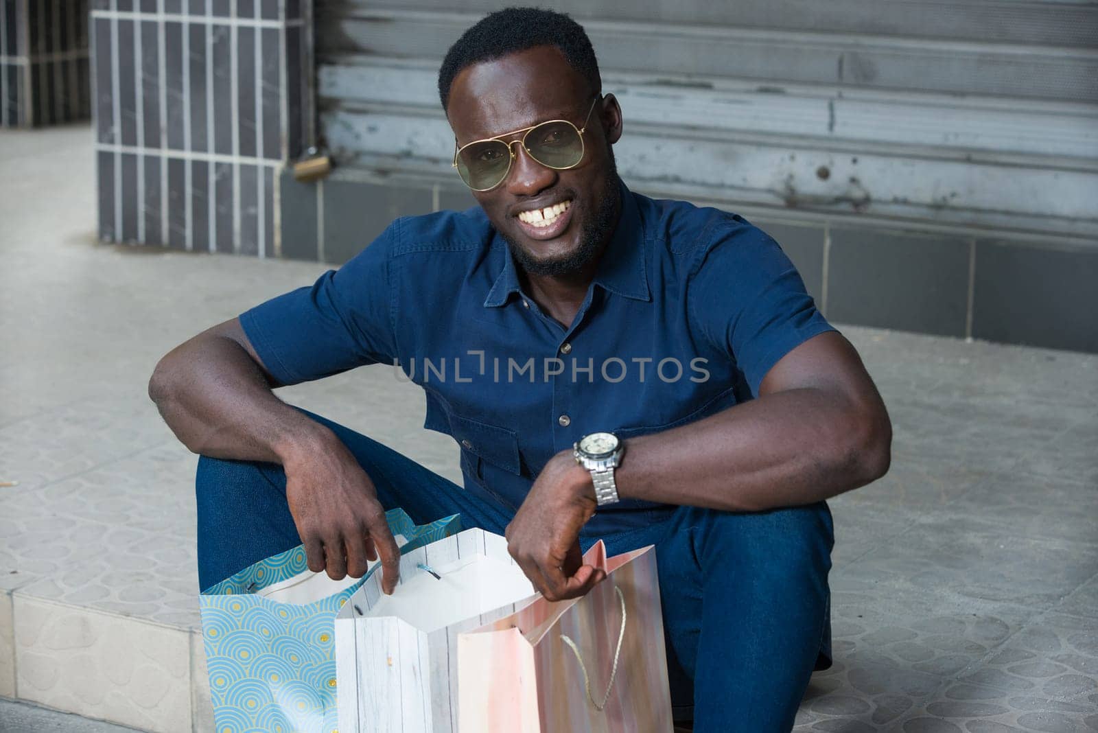 young man sitting outdoors with his shopping bag staring at the smiling camera.