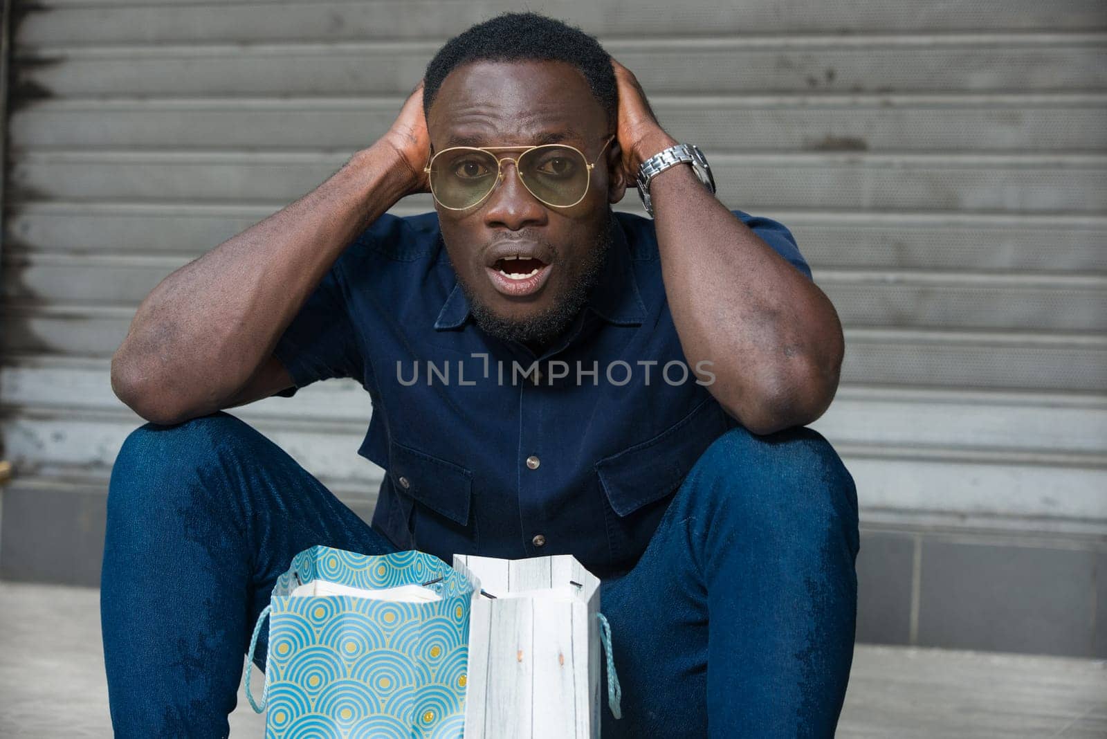 young man sitting on the floor thinking after shopping and looking at the camera.