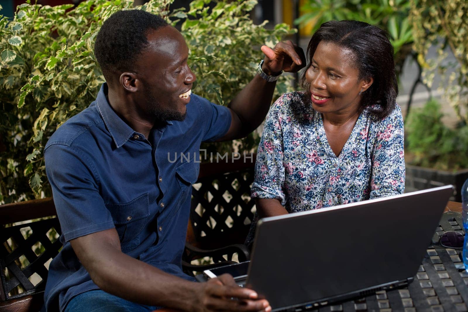 young couple sitting in a park with laptop watching each other smiling.