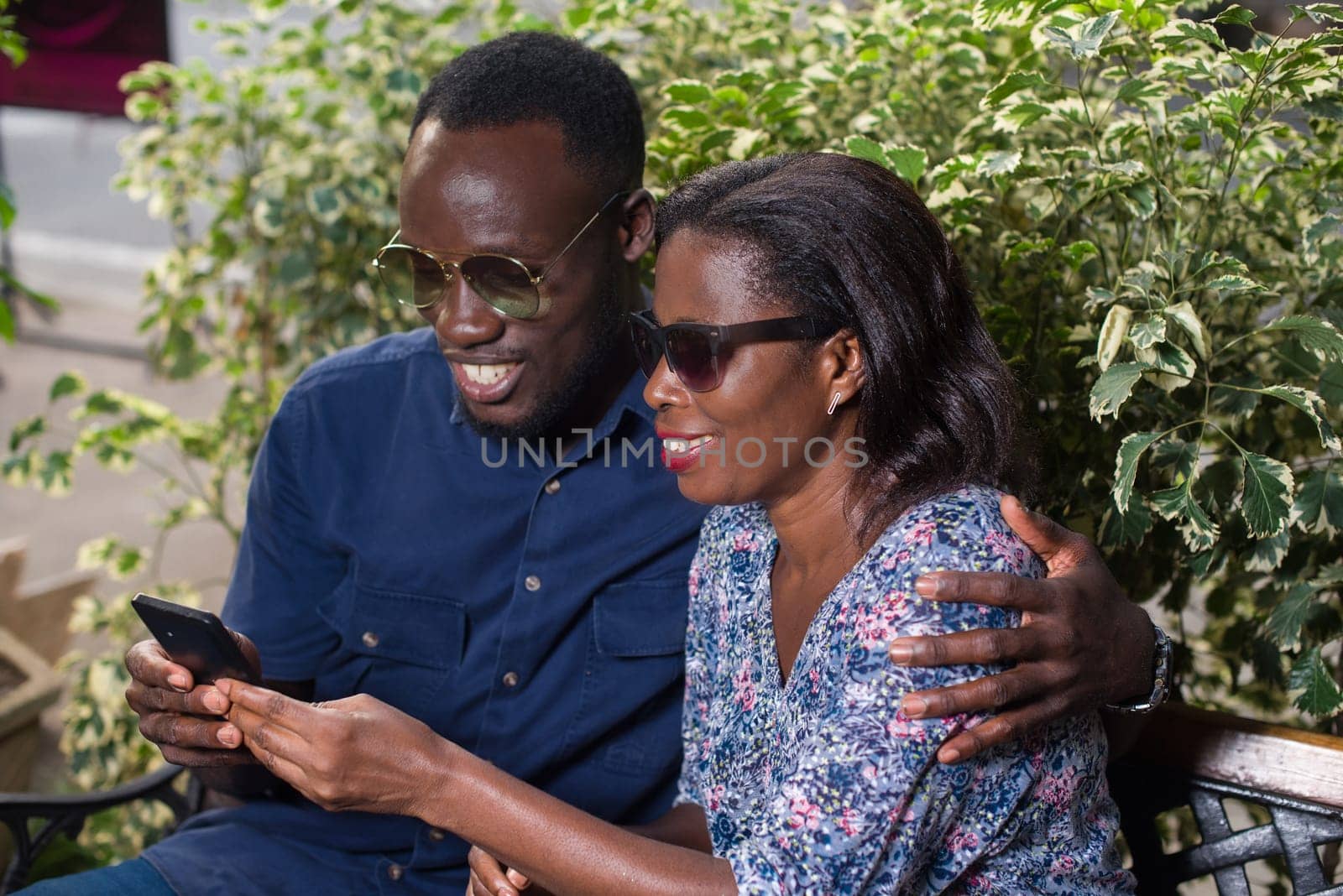 young couple sitting in a park looking at mobile phone while smiling.