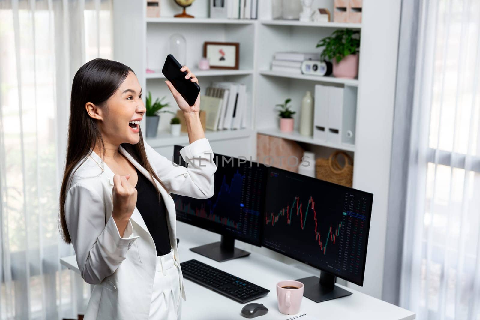 Successful Asian raising fist up, holding phone in profit stock. Stratagem. by biancoblue