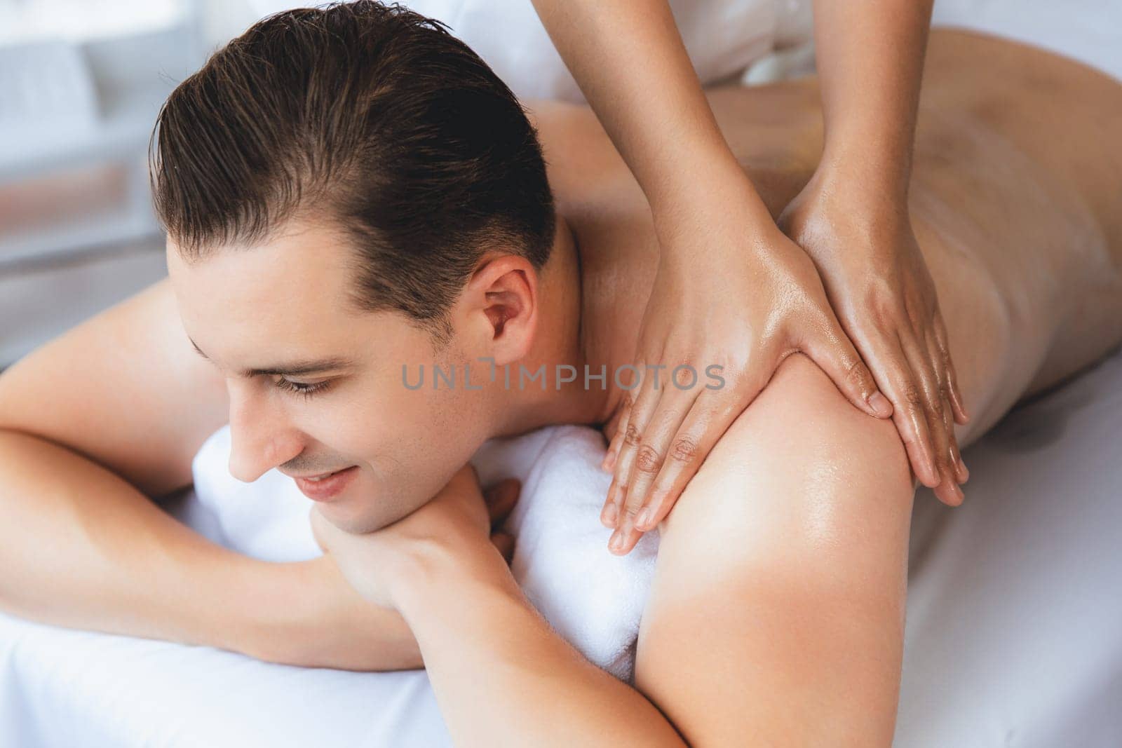 Caucasian man customer enjoying relaxing anti-stress spa massage and pampering with beauty skin recreation leisure in day light ambient salon spa at luxury resort or hotel. Quiescent