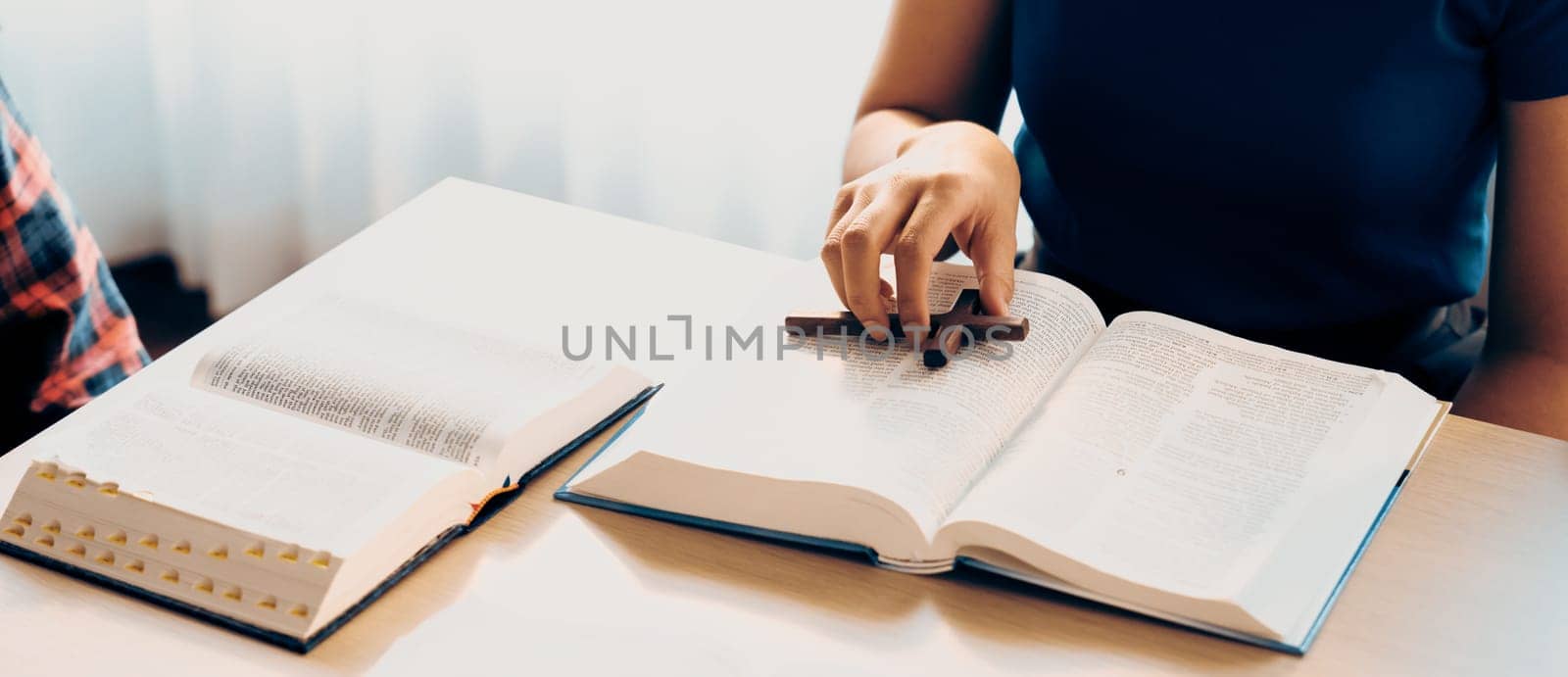 Close-up female Christian prayer pickup holy cross on bible book at wooden church table while asian believer reading bible. Concept of religion, faith, and god blessing. Warm background. Burgeoning.