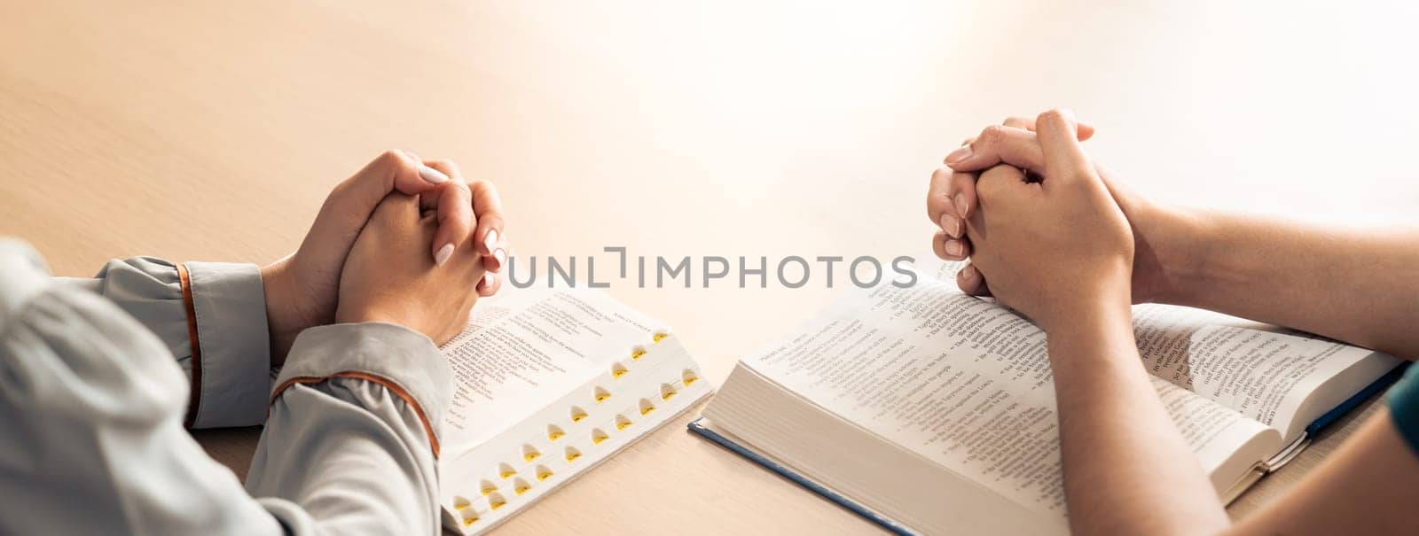 Two believer praying together on holy bible book faithfully with wooden cross placed at wooden church. Concept of hope, religion, faith, christianity and god blessing. Facing hand. Burgeoning.