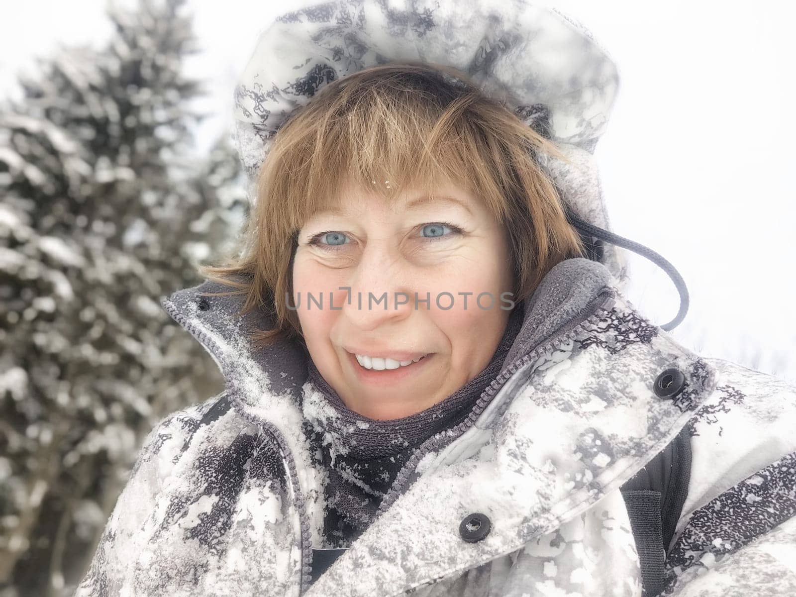 Cheerful middle aged woman in a winter warm sports jacket taking selfie on cold snow forest in nature outdoors