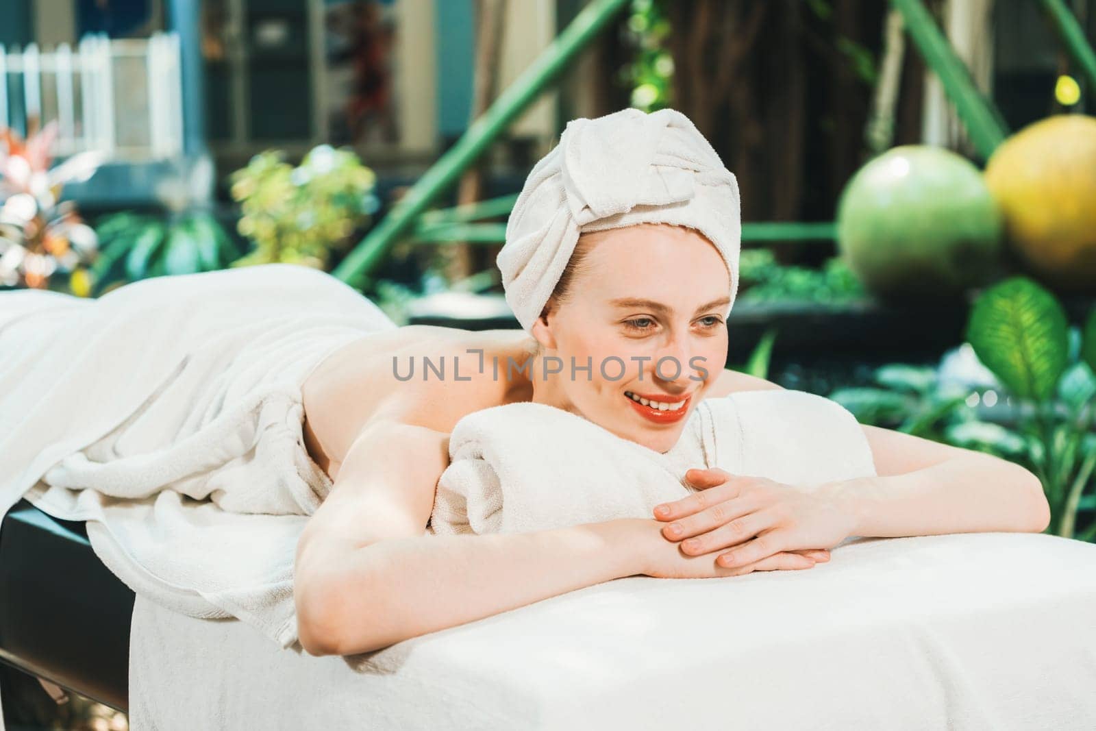 Beautiful young woman relaxes on a spa bed surrounded by nature. ready for a body massage. Attractive female in white towel lying peacefully during waiting for body massage. Close up. Tranquility