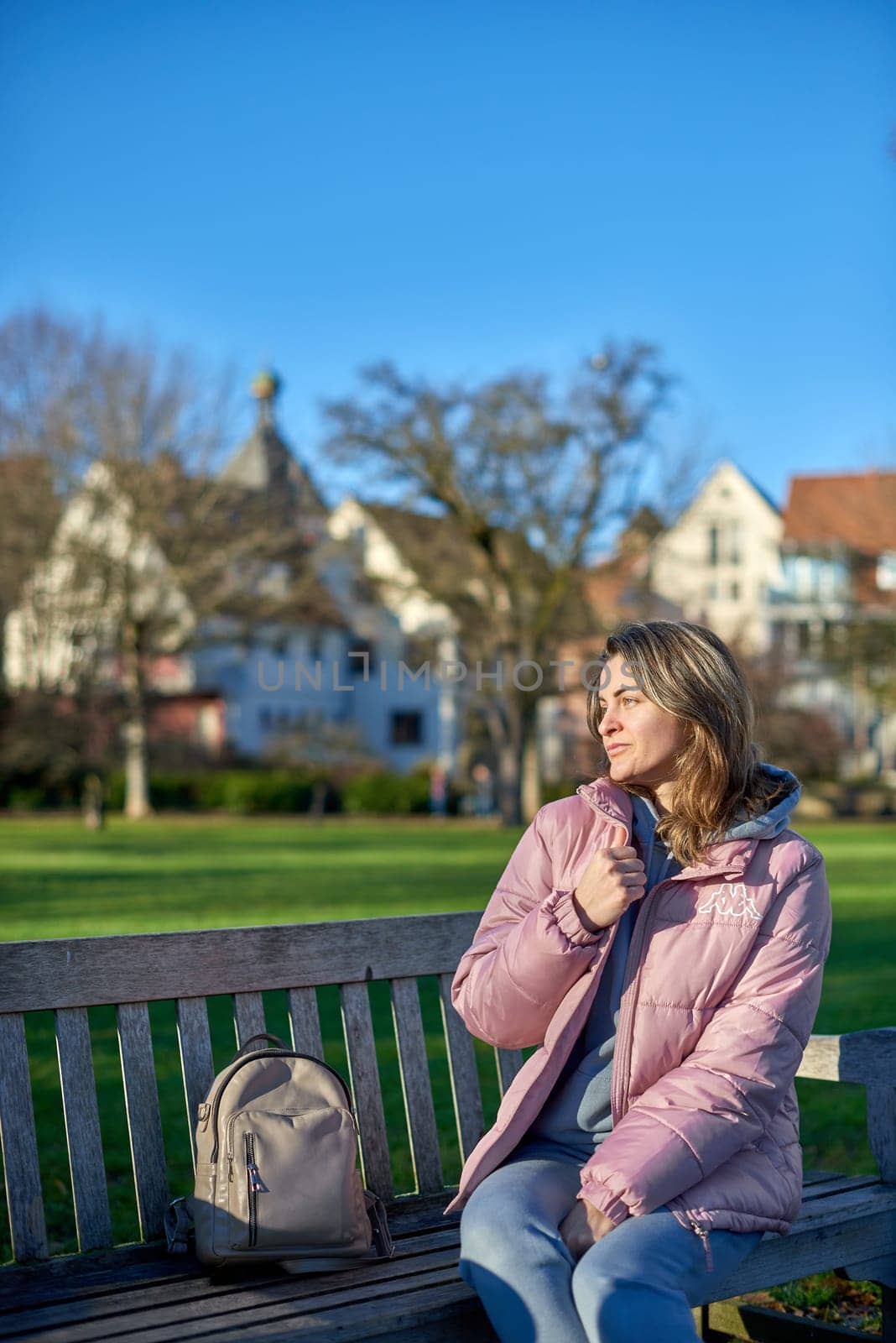 Winter Wonderland Elegance: Beautiful Girl in Pink Jacket Enjoys Festive Atmosphere in Bitigheim-Bissingen Park. girl in a pink winter jacket sits on a bench in a park against the backdrop of the historic town of Bitigheim-Bissingen, Baden-Württemberg, Germany. by Andrii_Ko