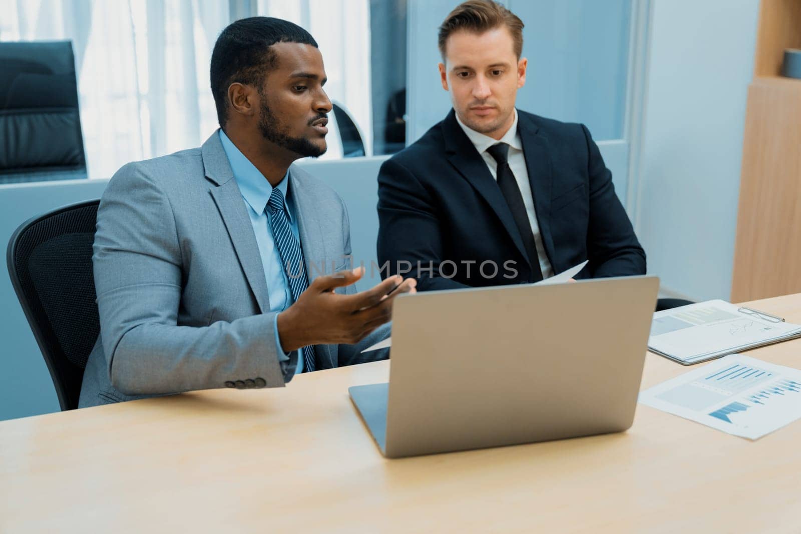 African male leader explain strategy while show solution to professional project manager by pointing at document, using laptop. Skilled business team brainstorming idea. Business meeting. Ornamented.