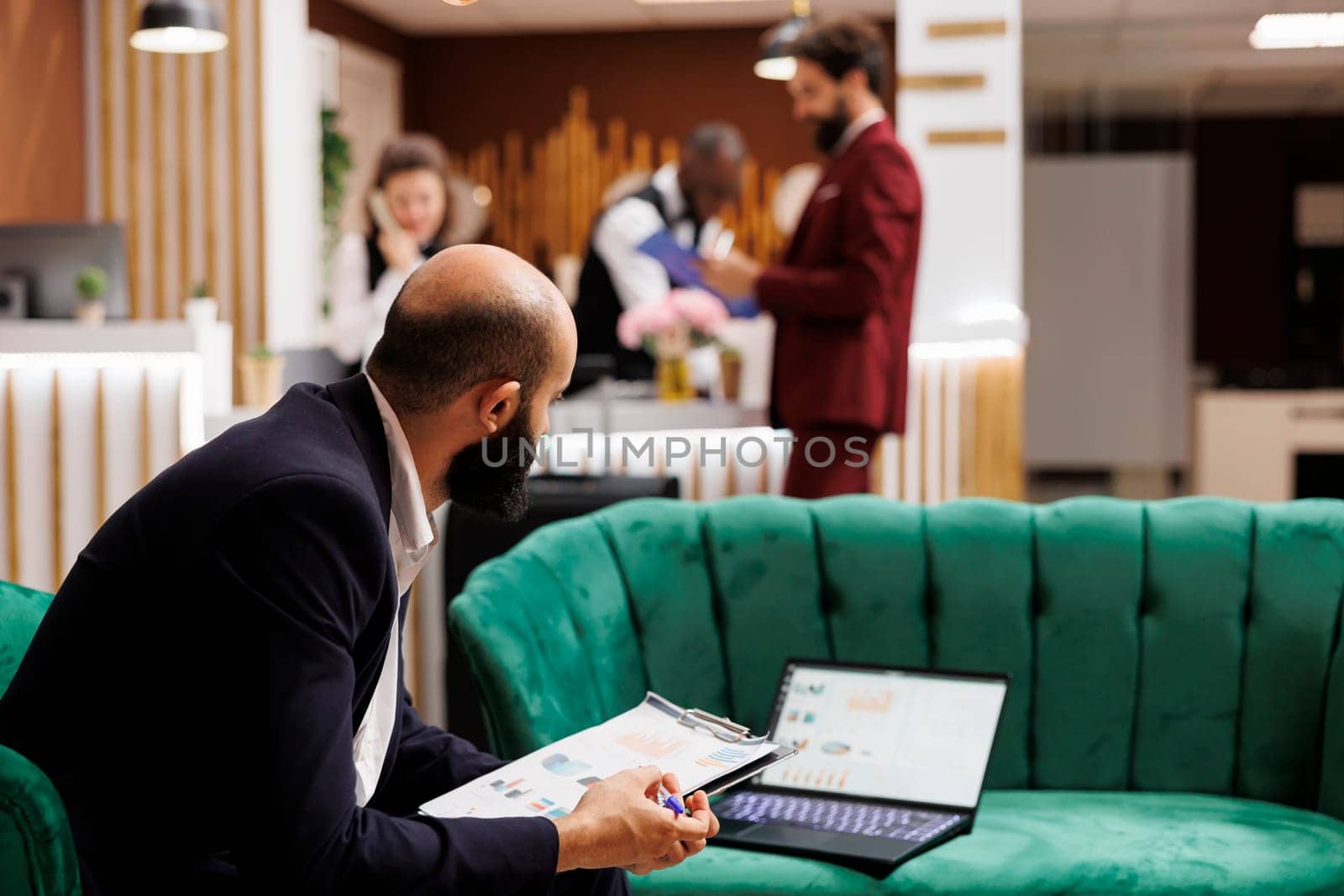 Businessman review documents in lobby at hotel, waiting to do check in procedure and killng time with office work. Entrepreneur attending official meeting and looking over speech notes.
