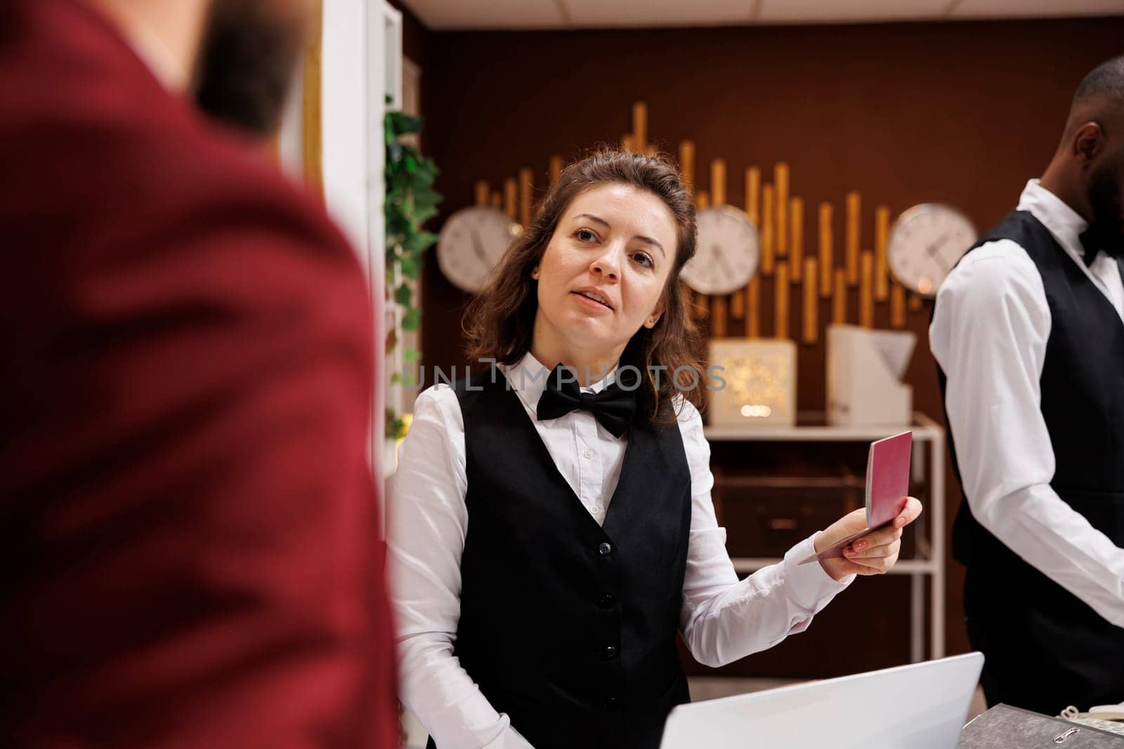 Hotel staff verifying passport for guest identification, preparing to do check in procedure in lobby. Receptionist looking at id papers after welcoming white collar worker on business trip.