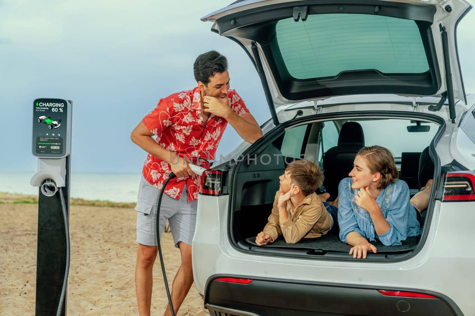 Family vacation trip traveling by the beach with electric car, lovely family sit on the trunk, charging EV car battery with green and sustainable energy. Family travel and eco-friendly car. Perpetual