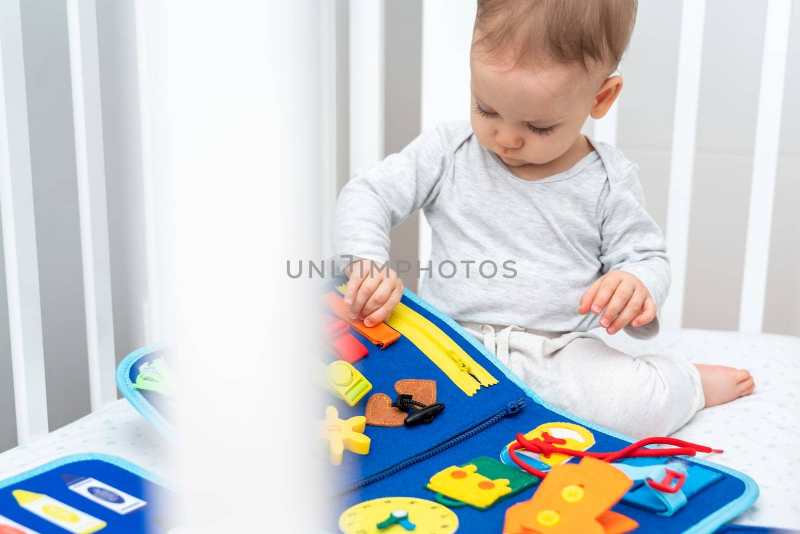 One year old baby playing with busy book sitting in crib