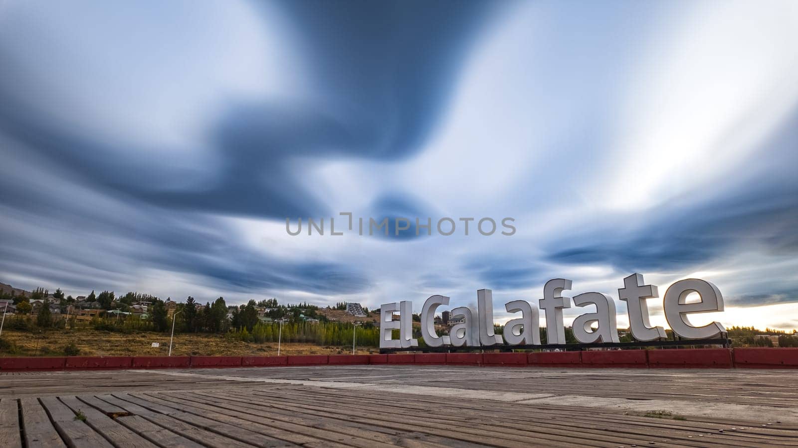 A long exposure photo captures dark, swirling clouds over the El Calafate sign, creating a dramatic scene.