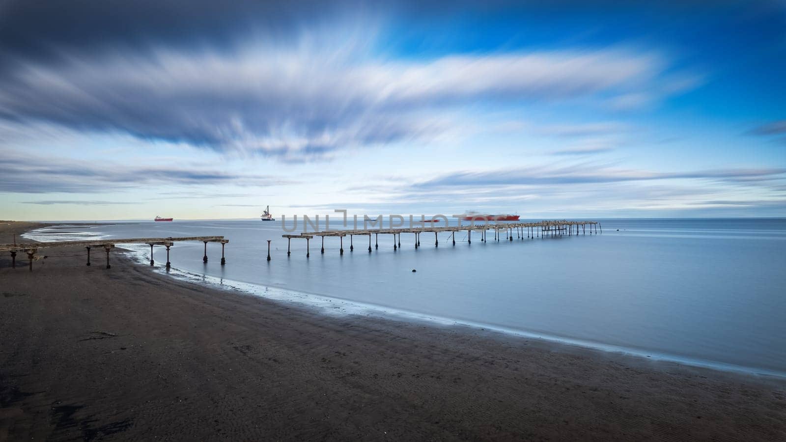 Tranquil sea with decaying pier captured in long exposure under dynamic clouds.
