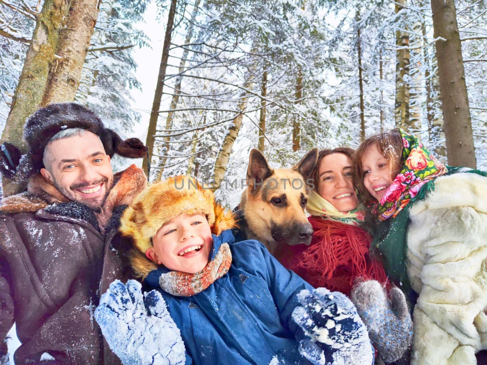 Joyful family ethnic dress with shawls and earflap hats and dog in winter forest in Russia carnival Maslenitsa. Tourists in Shrovetide in spring. Mother, father, son, daughter having fun in snow