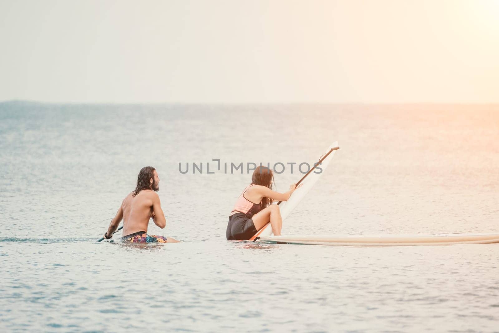 Sea woman and man on sup. Silhouette of happy young woman and man, surfing on SUP board, confident paddling through water surface. Idyllic sunset. Active lifestyle at sea or river