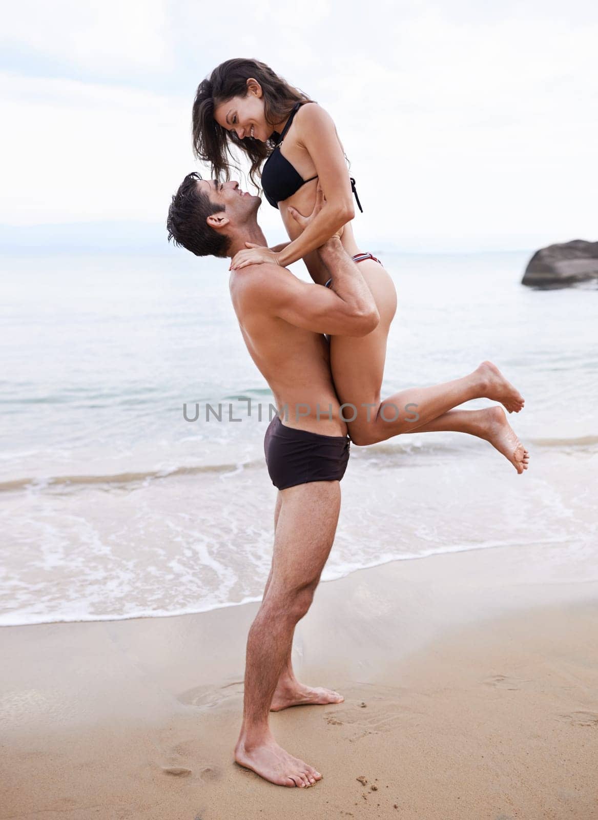 Playing, embrace and couple on beach with waves, travel adventure and relax on summer island holiday. Ocean vacation, woman and man hug in nature on date together with smile, love and romance in Bali.