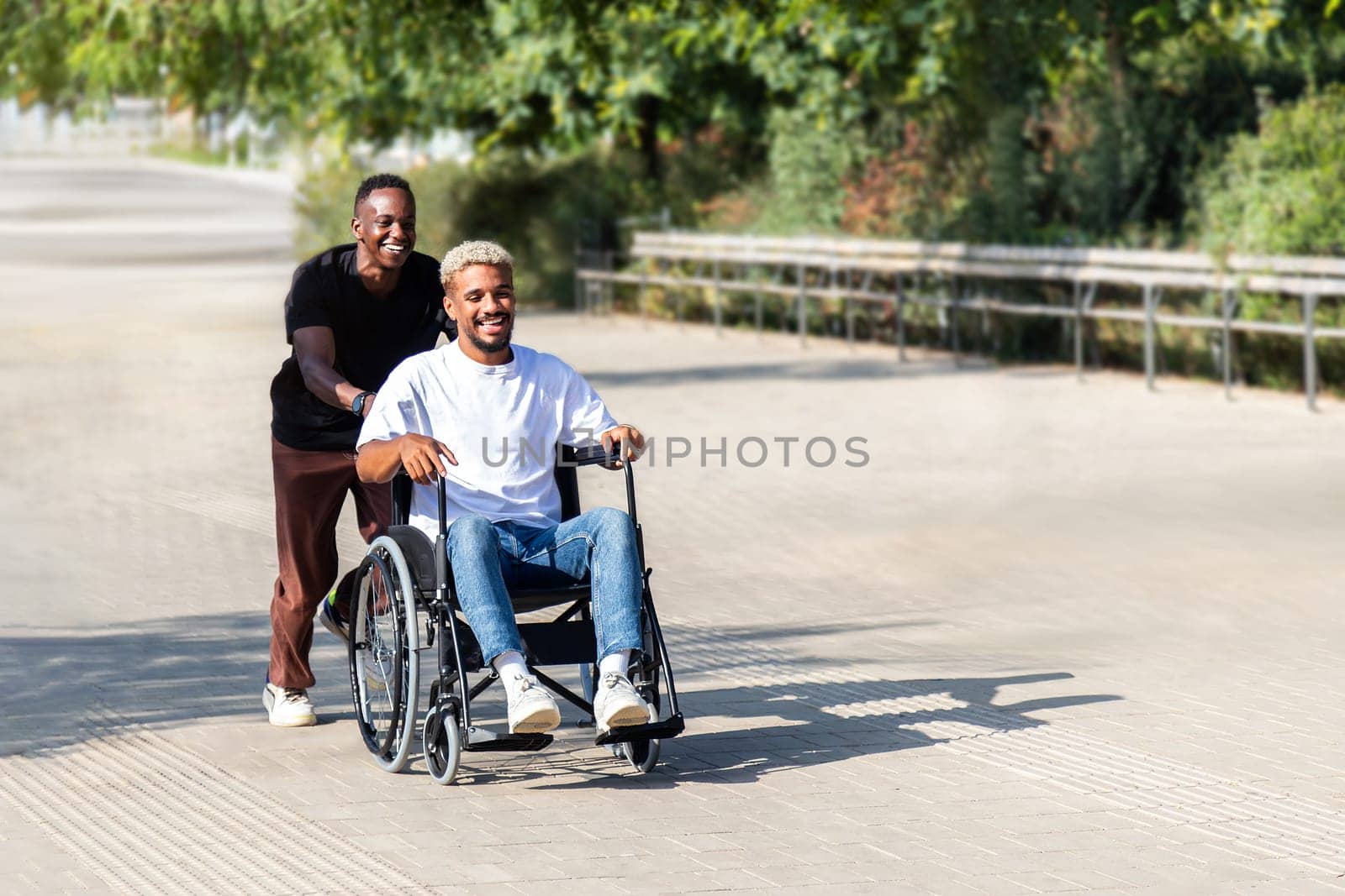 Black man running pushing his disabled African American male friend in a wheelchair in the city having fun. Copy space. by Hoverstock