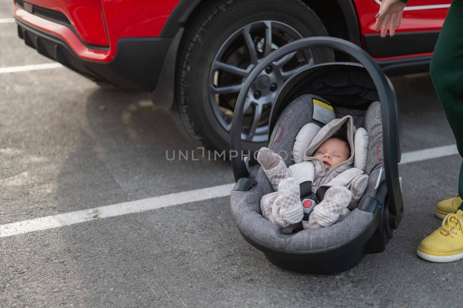 A Caucasian woman puts a child seat with a newborn baby in the car. Quick fastener