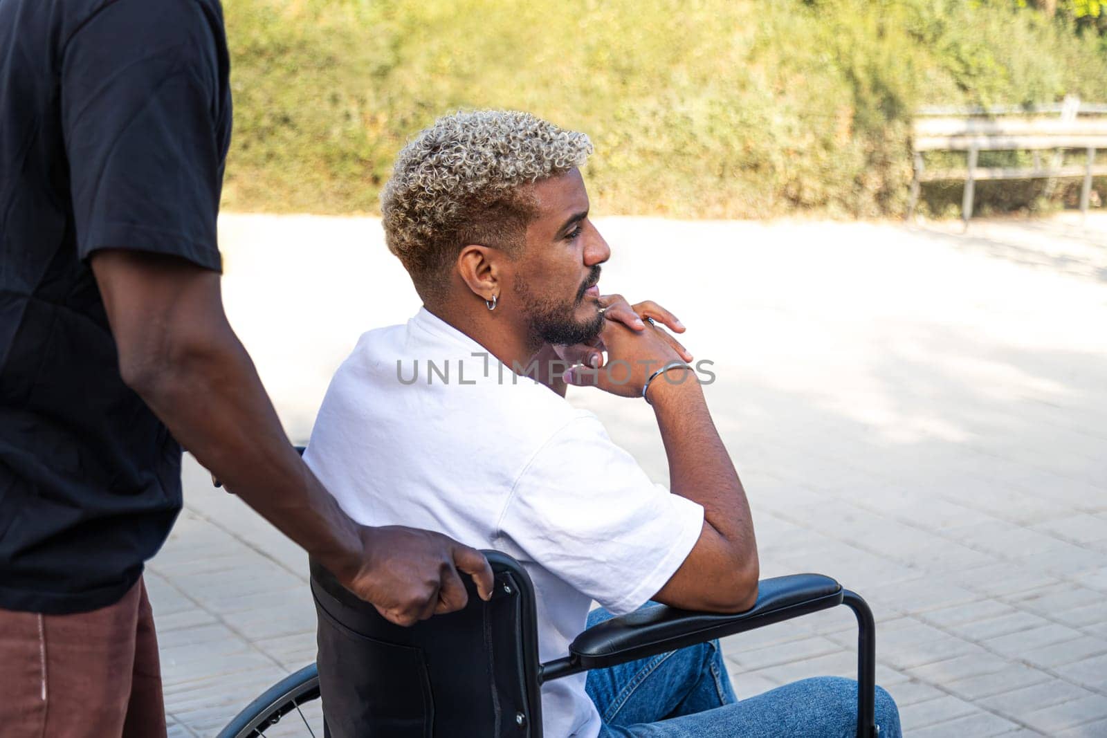 Side view of young disabled African American man in a wheelchair pensive looking away outdoors. Copy space. by Hoverstock