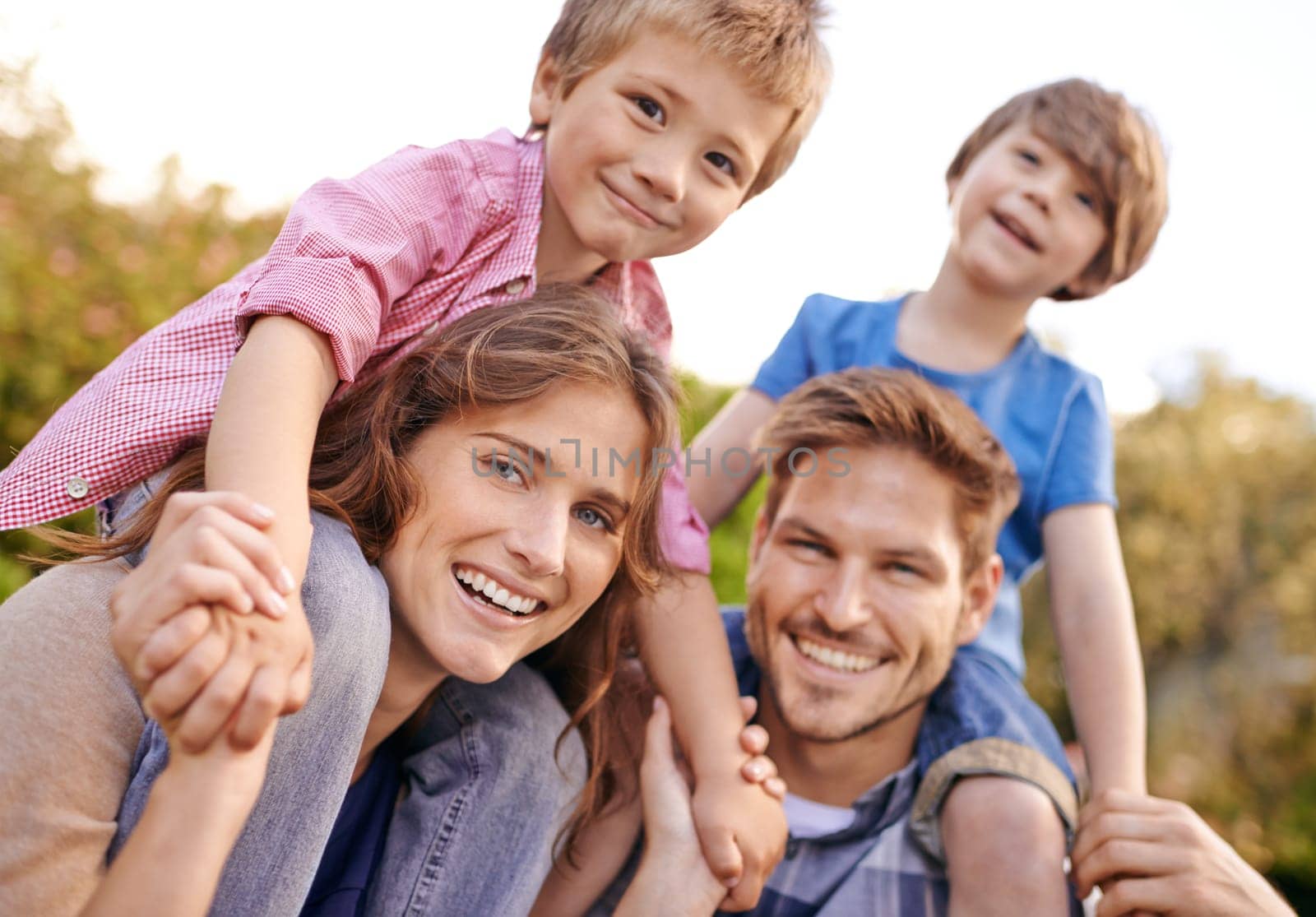 Happy, nature and children on parents shoulders in outdoor park or field for playing together. Smile, bonding and portrait of young mother and father carrying boy kids for fun in garden in Canada