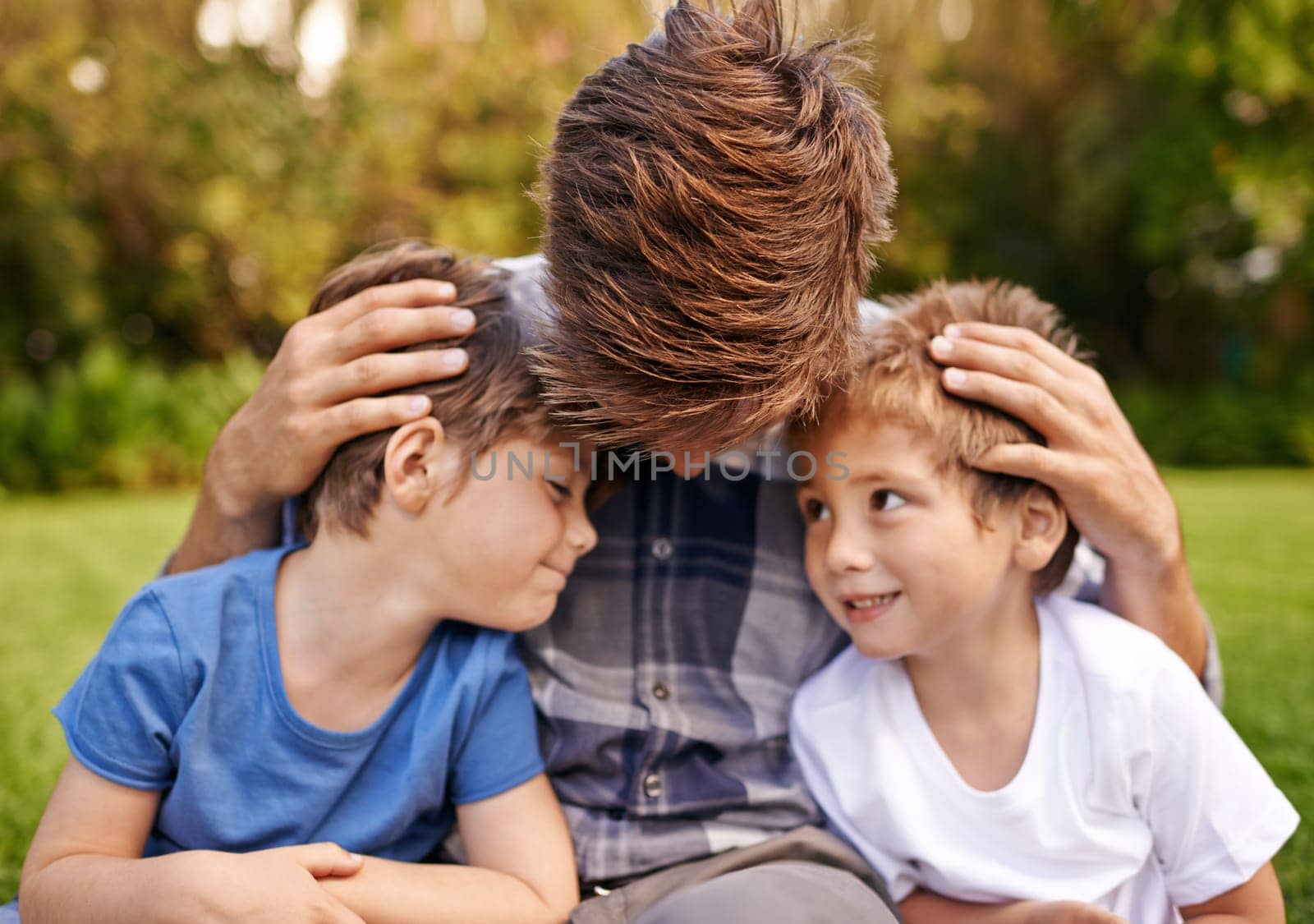Smile, nature and young children with father relaxing on grass in outdoor park or garden. Happy, love and excited boy kids sitting on lawn with dad for love, care and bonding in field together