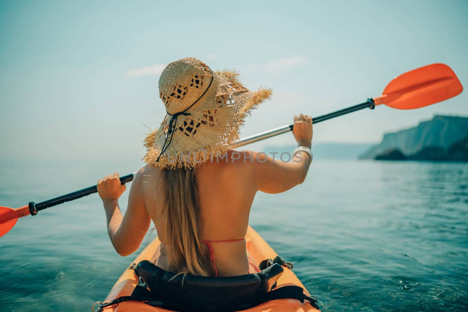 Woman in kayak back view. Happy woman with long hair in a swimsuit and hat floating in kayak on the sea. Summer holiday vacation. Summer holidays vacation at sea