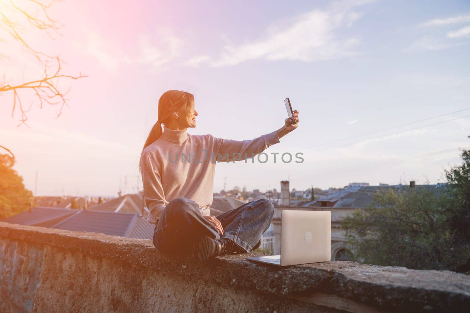 Woman freelancer uses laptop on cement wall outdoors against the sky and the roof of the city. The woman to be focused on her work or enjoying some leisure time while using her laptop