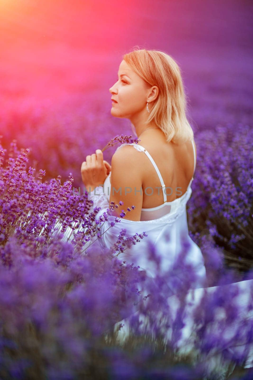 Woman lavender field. A middle-aged woman sits in a lavender field and enjoys aromatherapy. Aromatherapy concept, lavender oil, photo session in lavender.