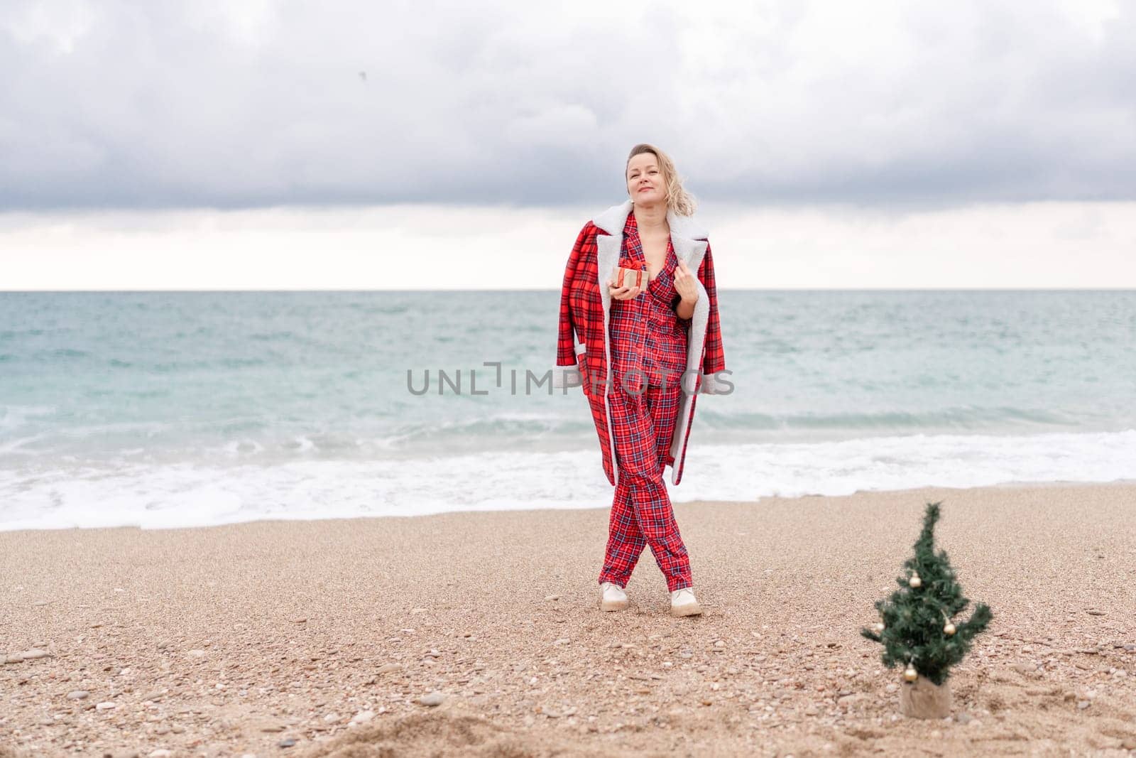 Lady in plaid shirt holding a gift in his hands enjoys beach with Christmas tree. Coastal area. Christmas, New Year holidays concep.