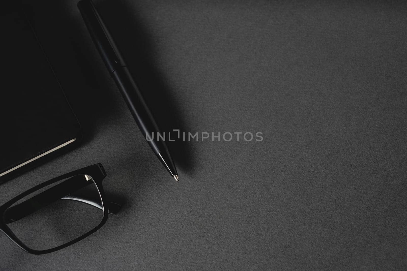 Top view of ballpoint pen, glasses and notepad lying on dark gray table by Sonat