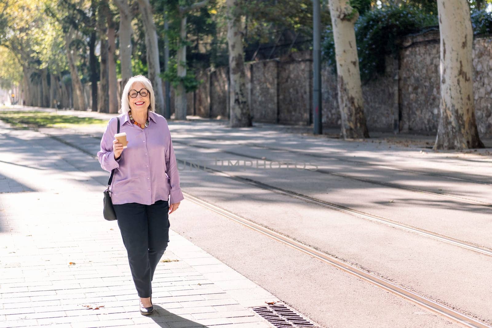 senior woman walking on the street holding a takeaway coffee in her hand, concept of elderly people leisure and active lifestyle