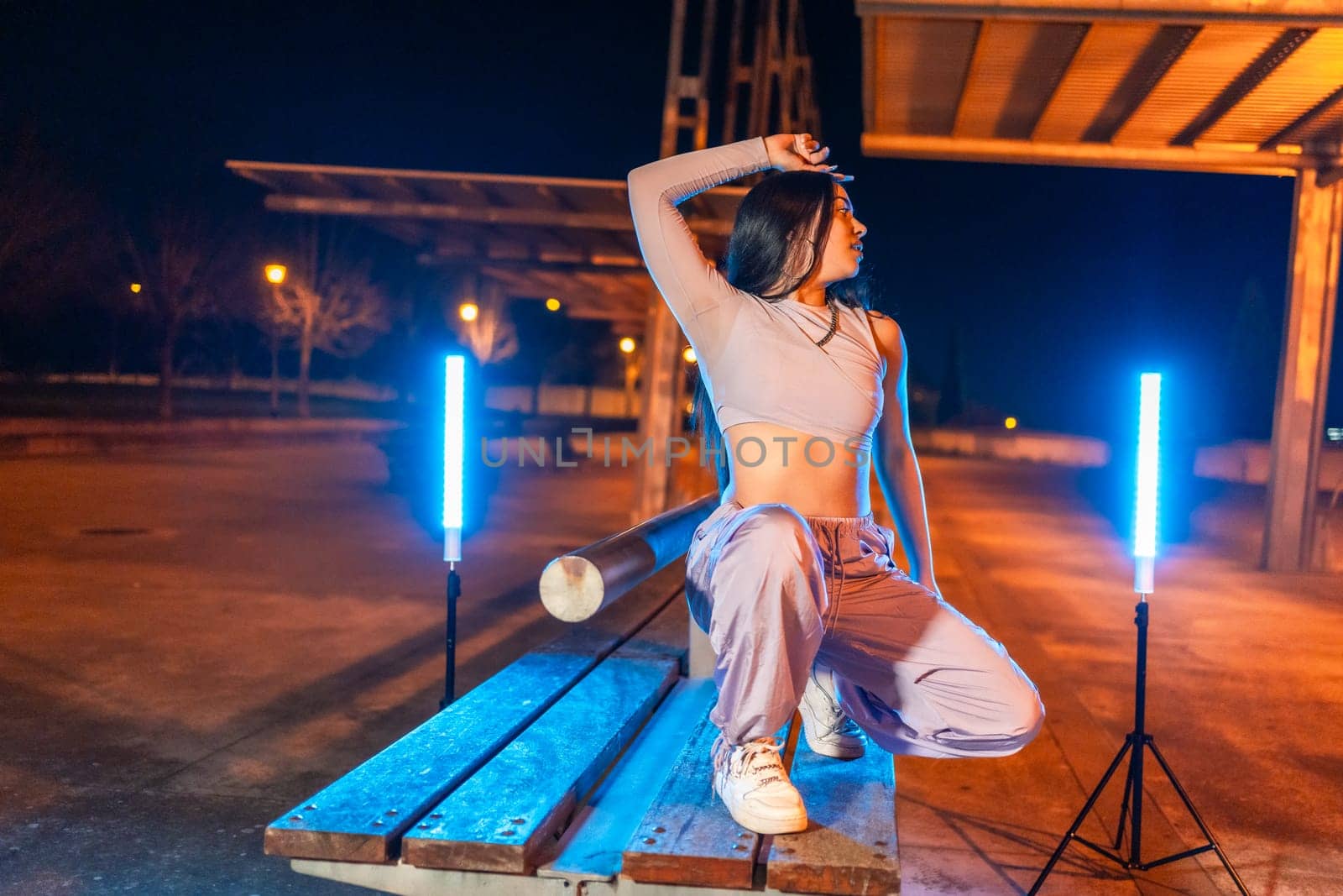 Sensual cool rap artist crouching and posing in a park at night surrounded by neon lights