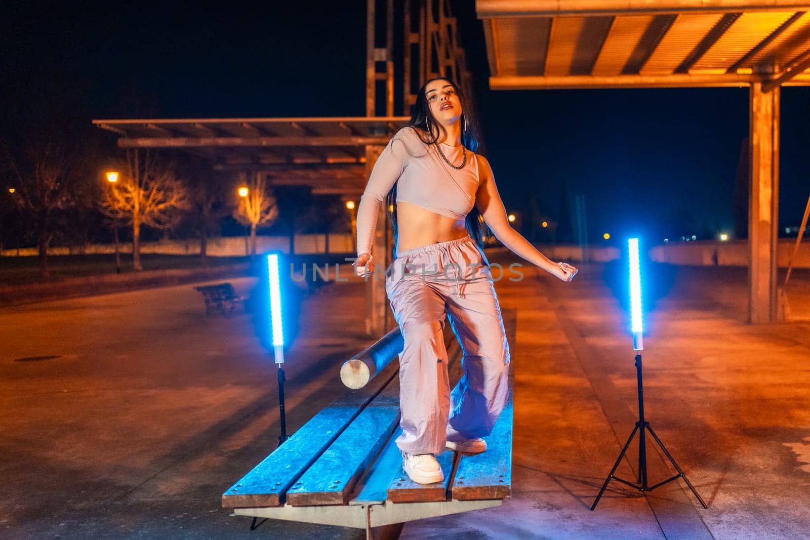 Portrait of a trap artist dancing on a park table at night surrounded by neon lights