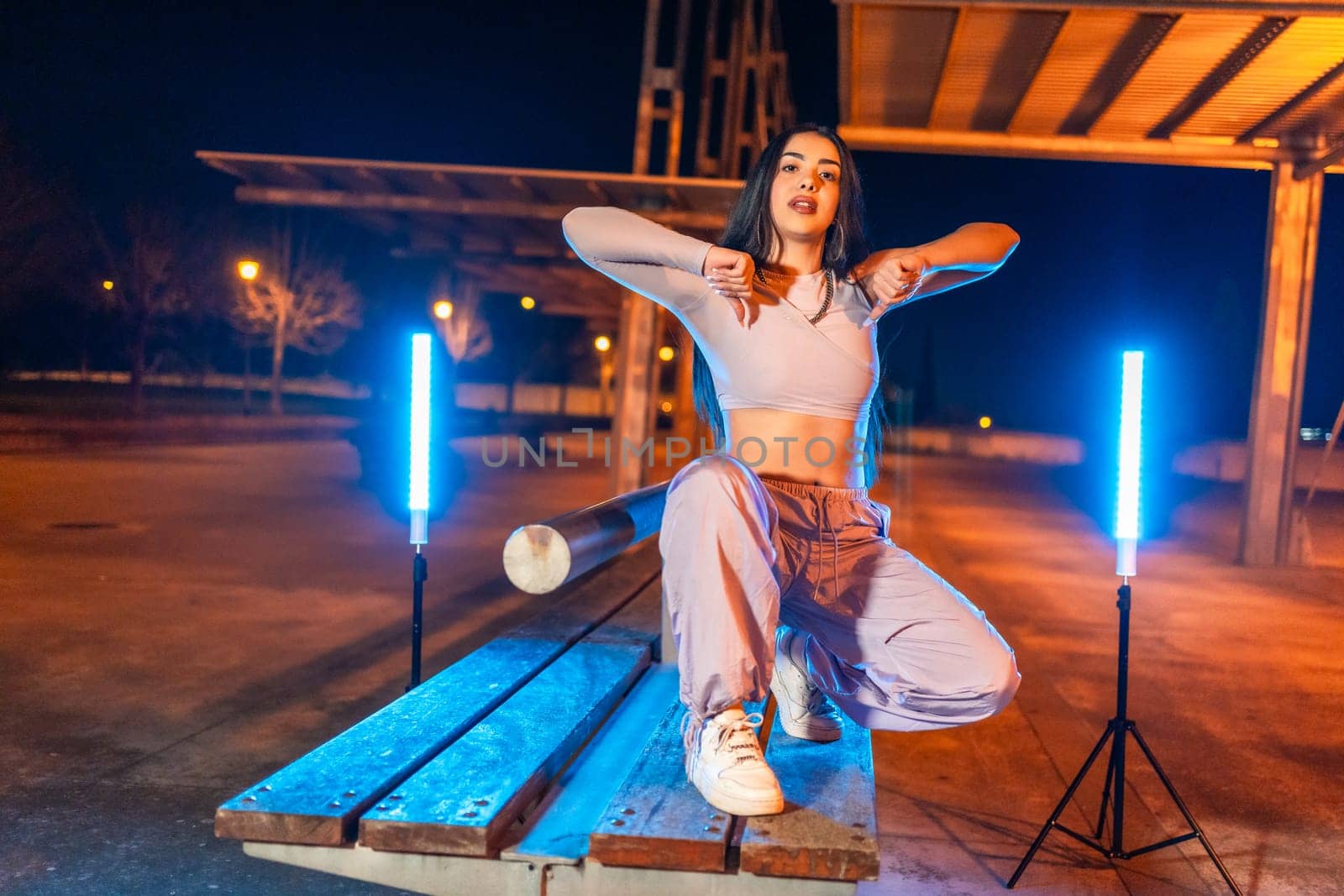 Confident trap artist posing crouching outdoors at night next to neon lights