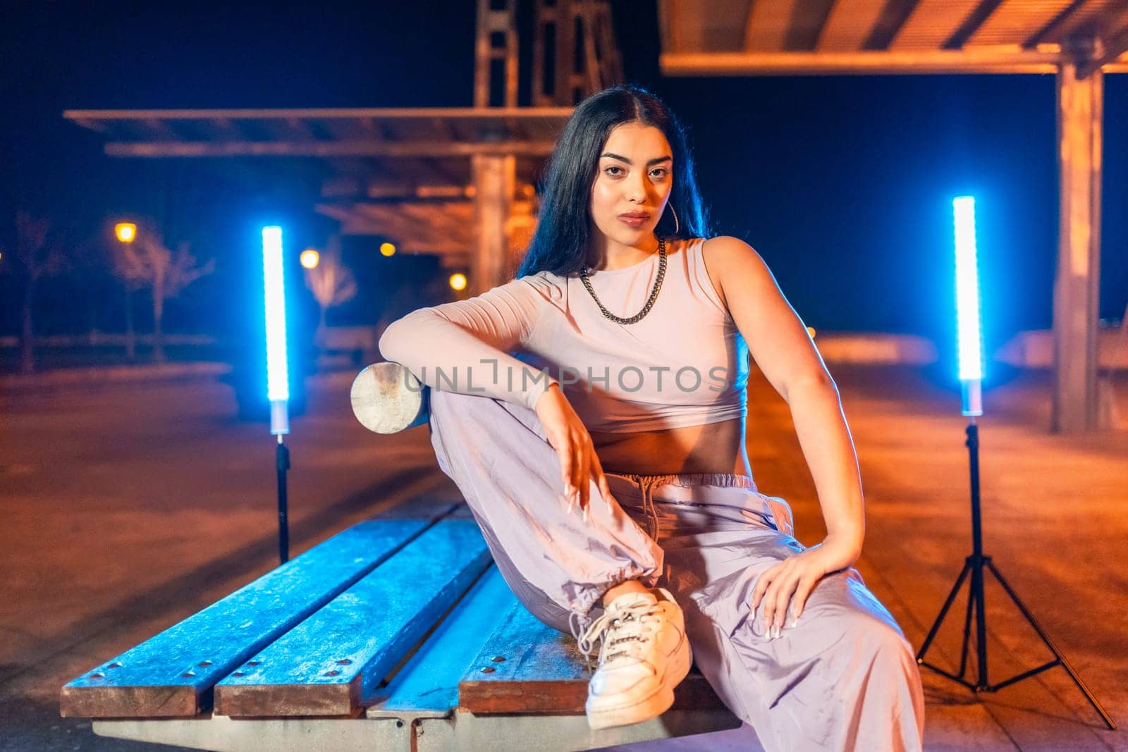 Young dancer sitting posing at night sitting in an outdoor park next to neon lights