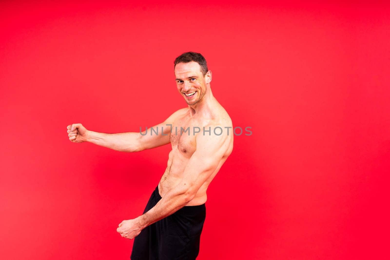 Image of muscle man posing in a studio, dark white red background