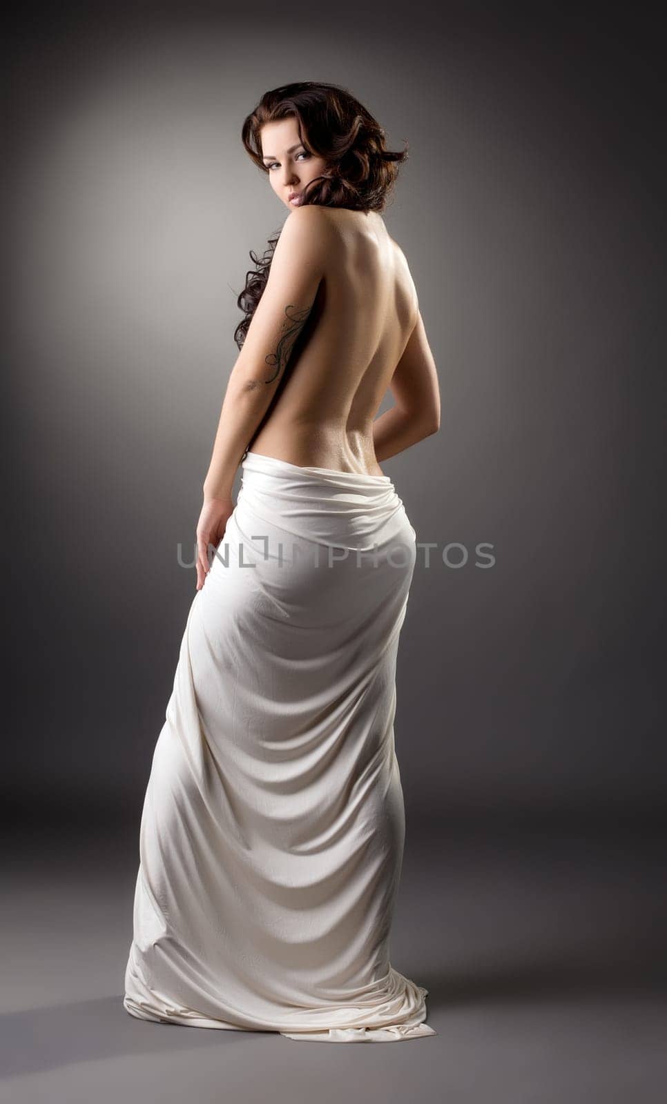 Back view of slender brunette posing at camera, on gray background