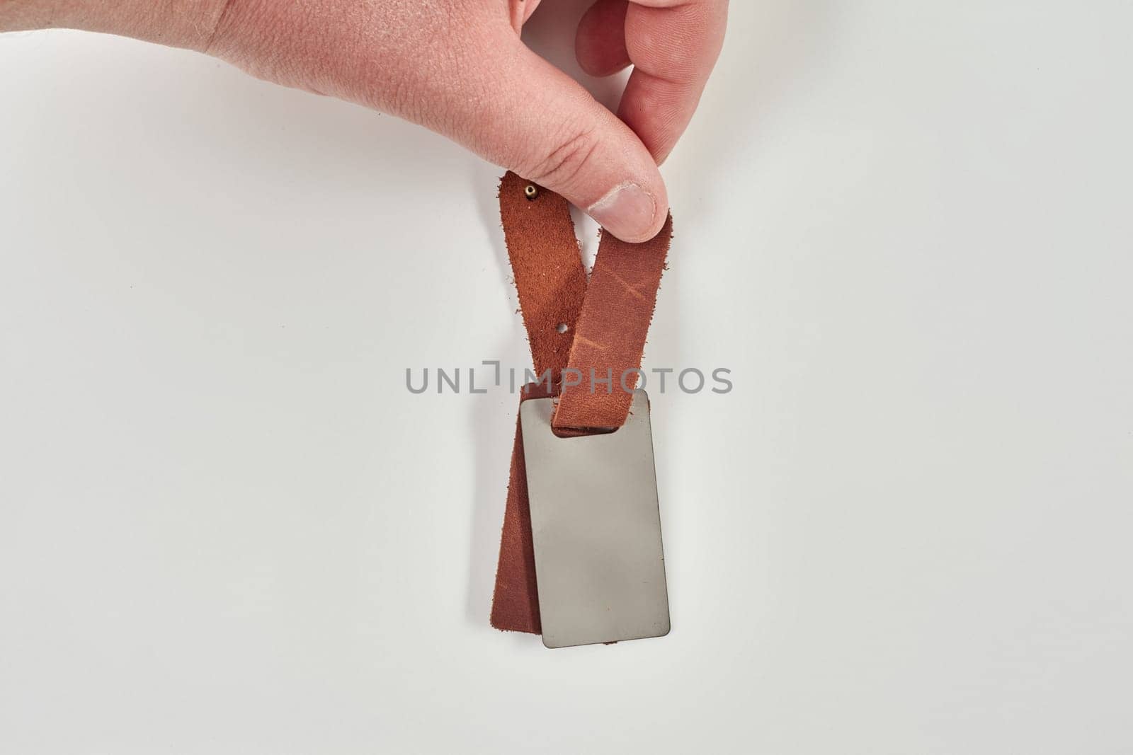 Male hand presenting unmarked brown leather keychain designed for photo imprinting or custom engraving, against light backdrop with copyspace. Stylish handcrafted accessories