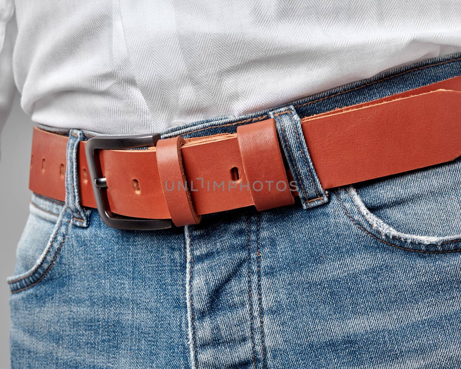 Closeup of terracotta leather belt with custom DAD embossing on loop complementing casual look of man dressed in jeans and white shirt. Concept of quality craftsmanship and personalized gifting