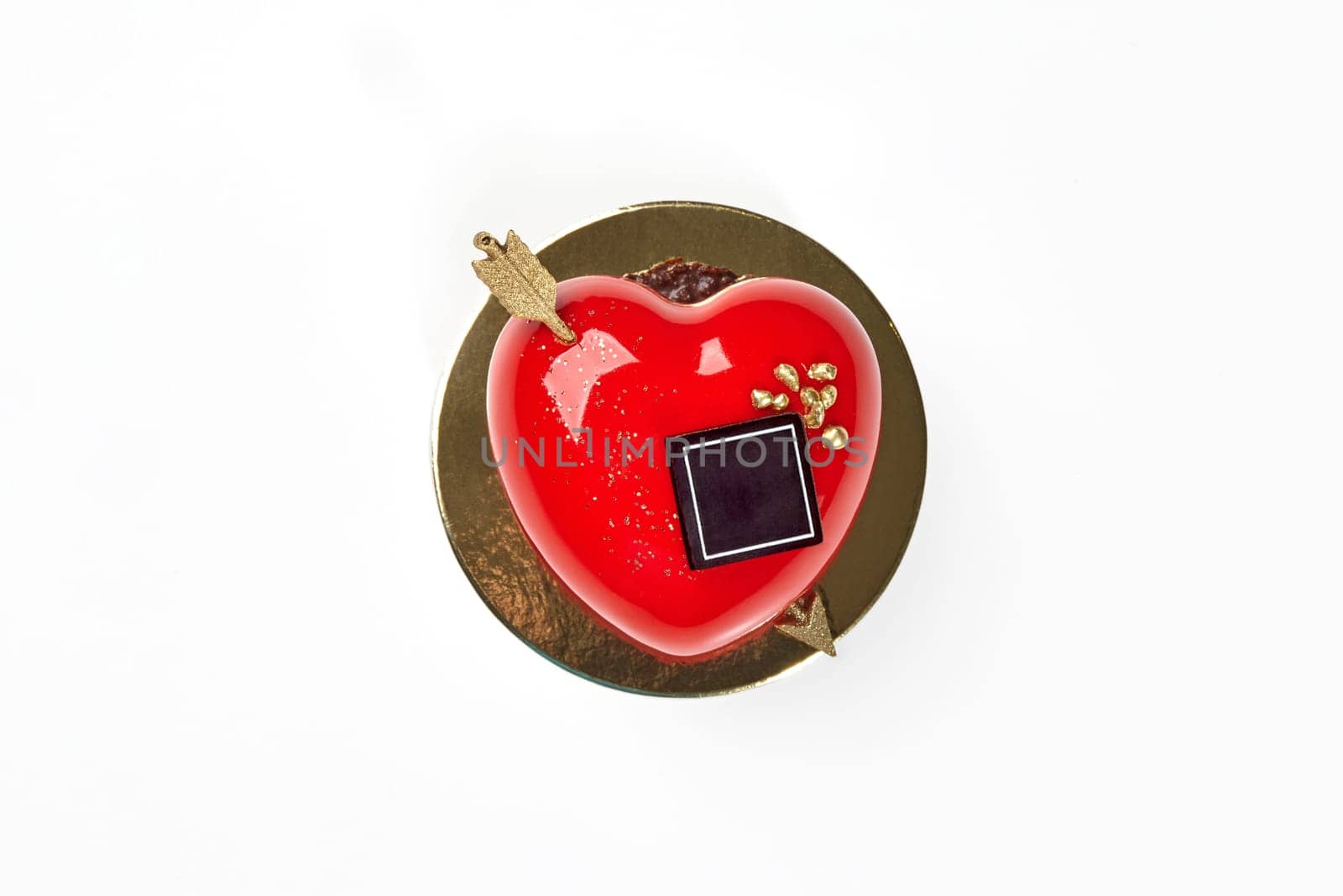 Vibrant red heart-shaped strawberry mousse cake with glossy icing, chocolate and gold arrow, perfect for celebrations of love and affection on Valentines Day, top view against white background
