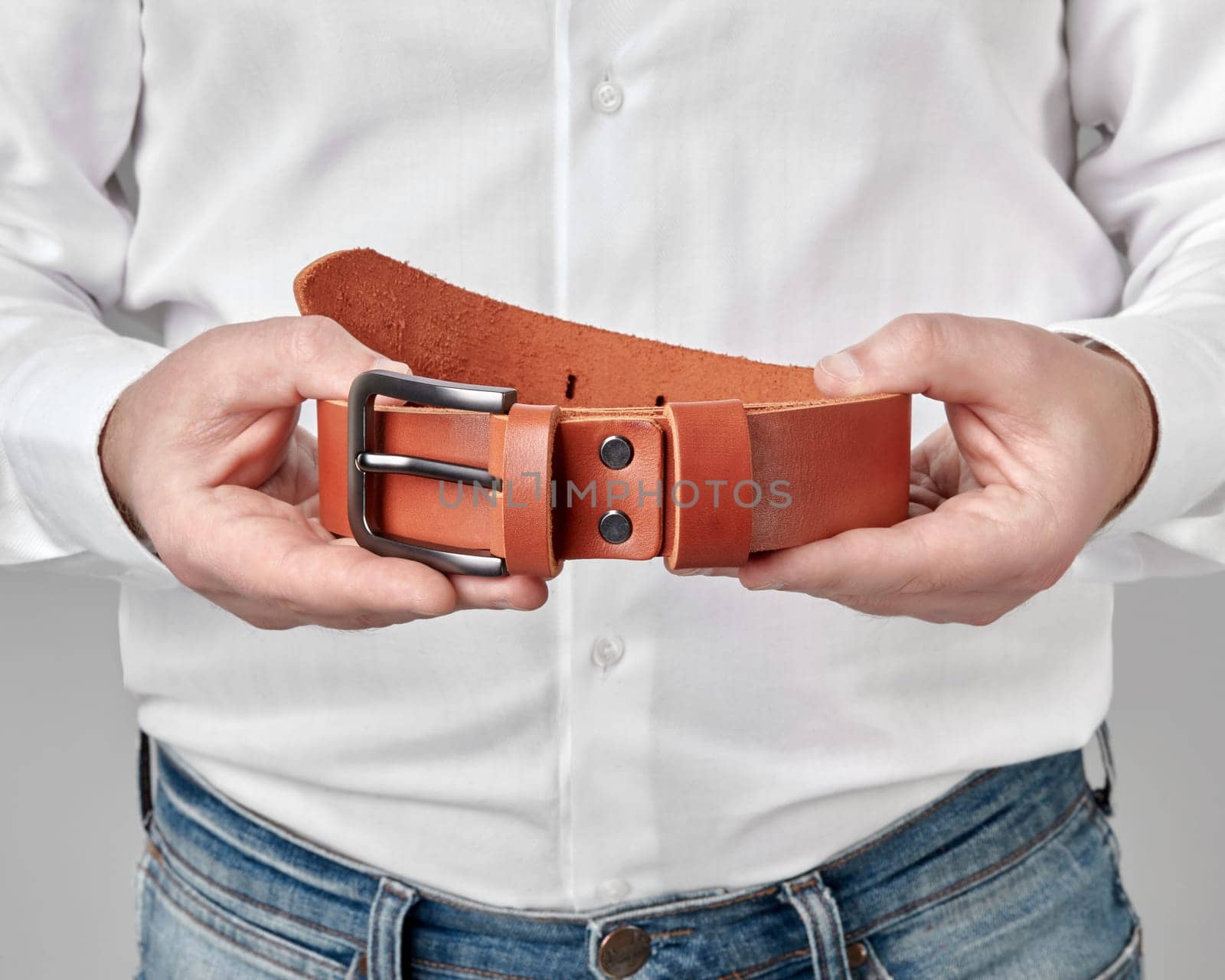Male hands holding terracotta leather belt with custom DAD embossing on loop, cropped shot. Stylish personalized handcrafted accessory complementing mans everyday look