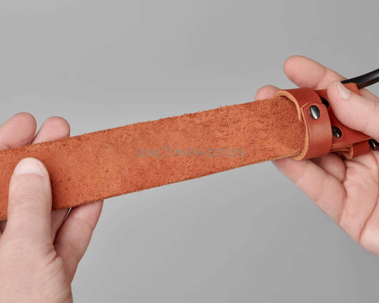 Close-up of terracotta leather belt engraved with inspirational quote by Edward Young in male hands, symbolizing thoughtful gifting and literary passion