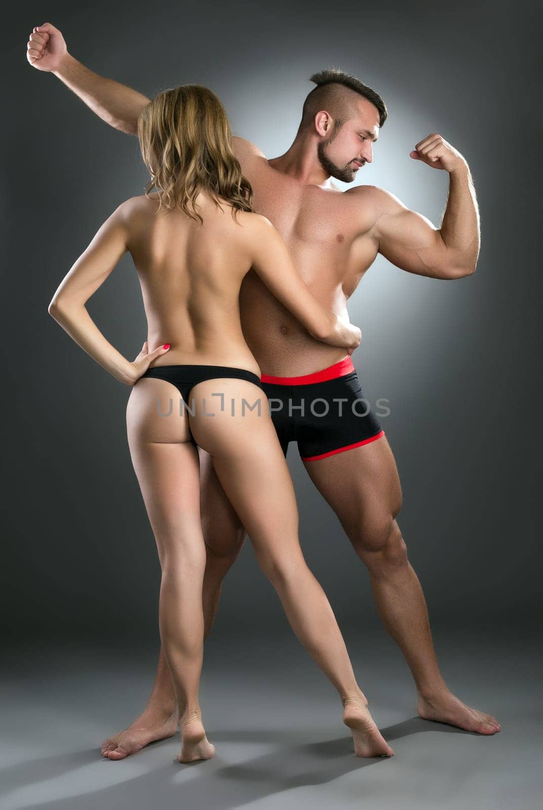 Strong guys attract sexy girls. Studio shot, on grey backdrop