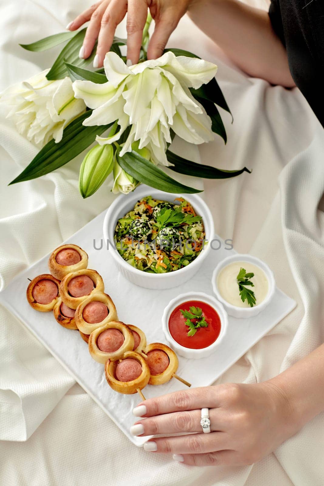 Female hands arranging lilies beside gourmet snack platter by nazarovsergey