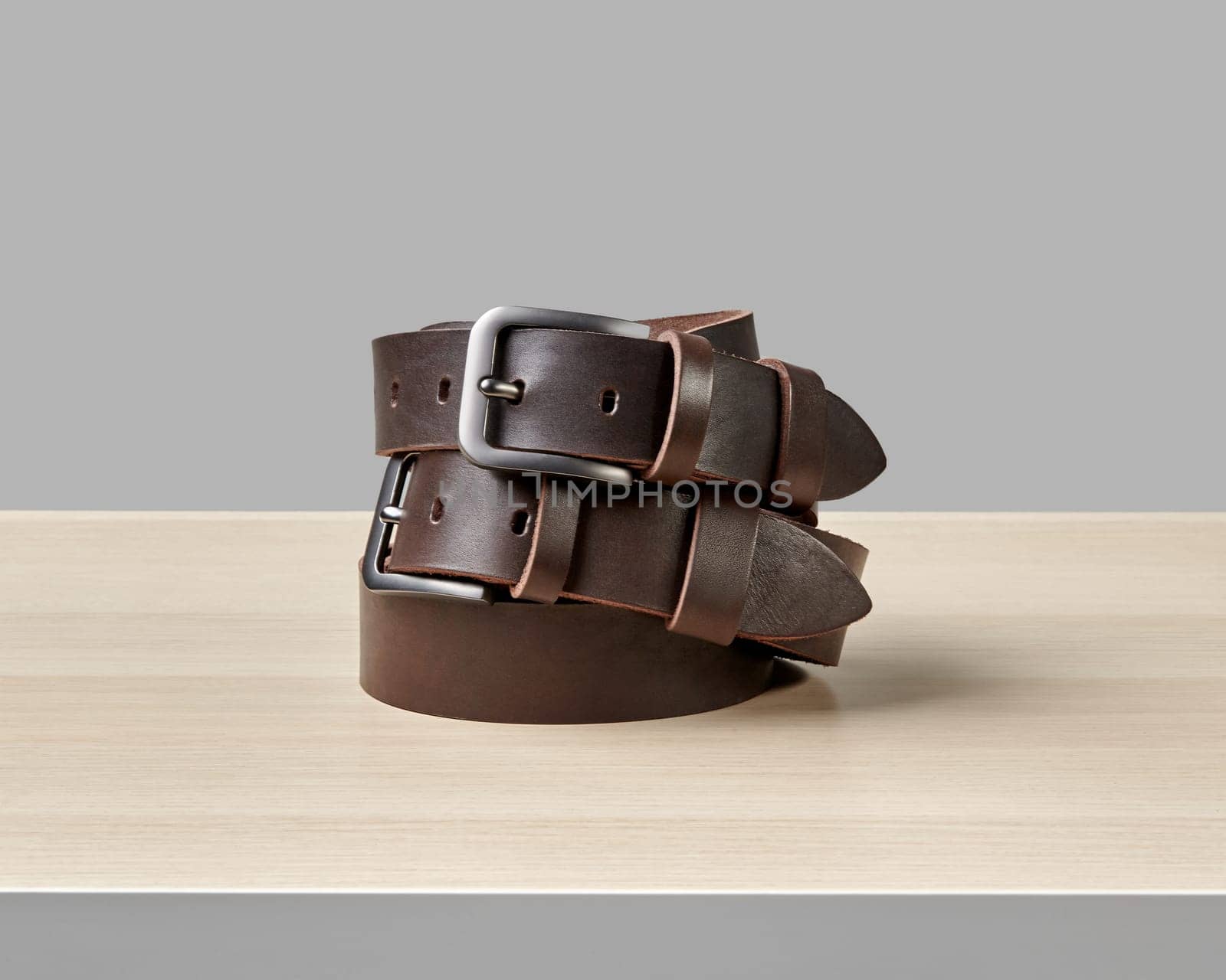 Two custom dark brown leather belts with stylish buckles and DAD embossed on loop folded on wooden table. Concept of quality craftsmanship and personalized gifts
