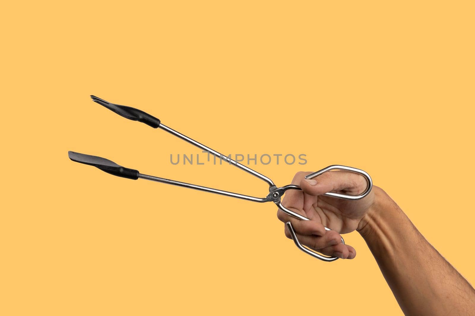 Male hand holding kitchen tong isolated on yellow background. High quality photo