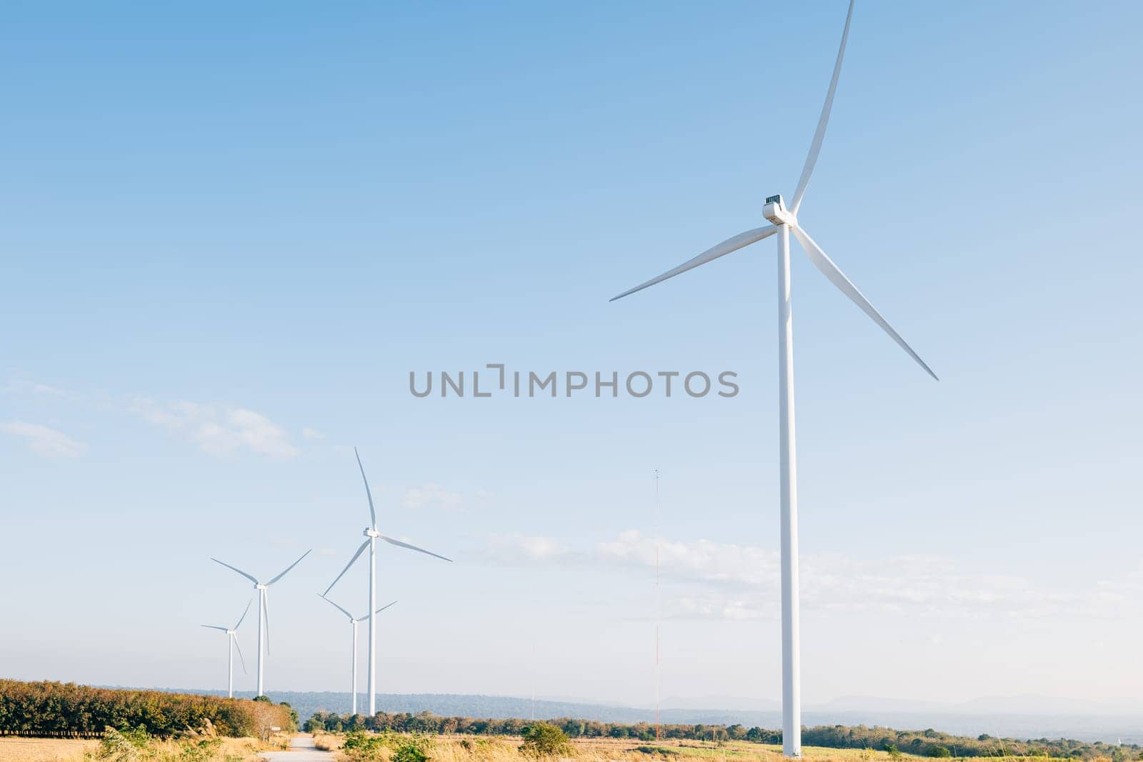 In a scenic prairie windmill farm turbines generate clean power on a mountain. A symbol of sustainable development and innovative wind technology against a blue sky.