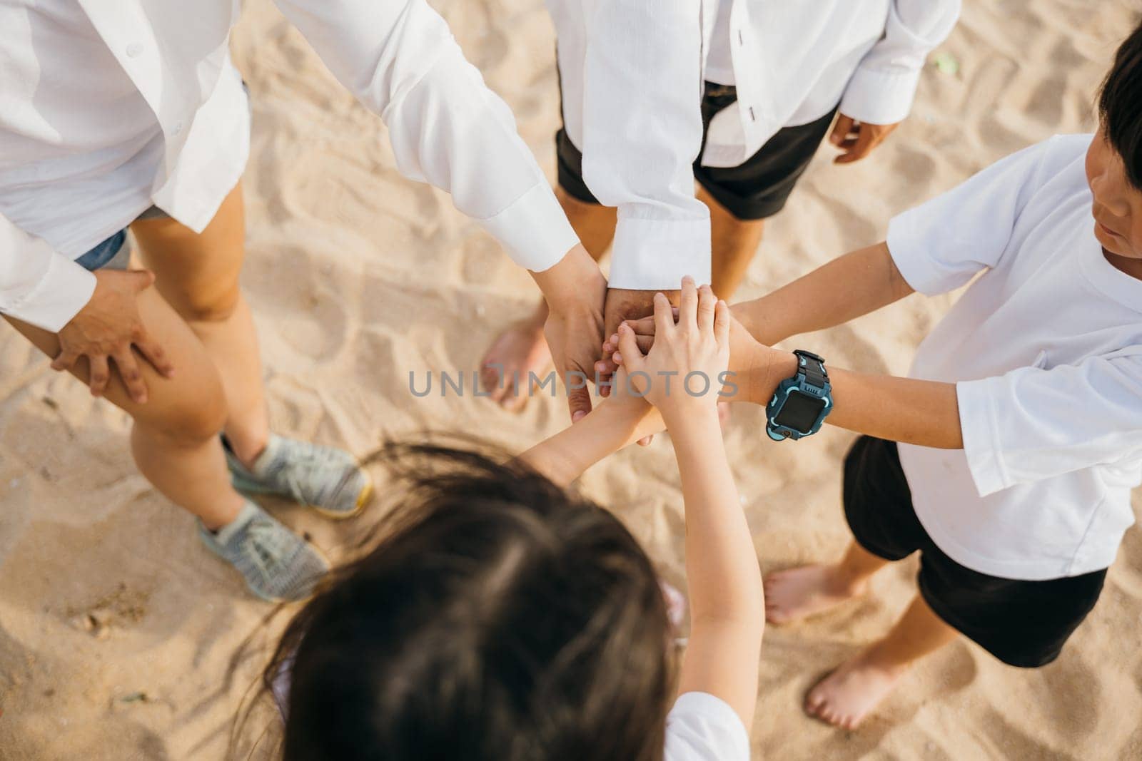 Beach teamwork with a happy family. Hands together in a stack symbolizing success and achievement. Parents and children unite in nature emphasizing community motivation and togetherness by Sorapop